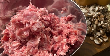 Raw ground Italian sausage in a bowl with chopped mushrooms and burger buns, ready for cooking a hearty meal.