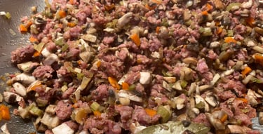 Close-up of savory ground meat, mushrooms, and vegetables cooking in a pan, featuring bay leaves for rich flavor.
