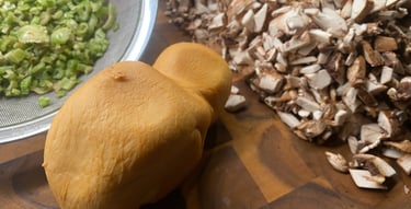Smoked mozzarella cheese, chopped mushrooms, and sliced celery on a wooden cutting board for cooking preparation.