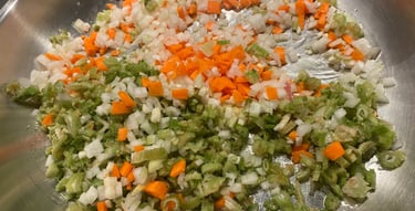 Finely diced carrots, celery, and onions sautéing in a stainless steel pan as a mirepoix base.