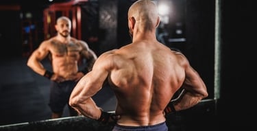 Muscular bodybuilder flexing back muscles and lats in front of a gym mirror.