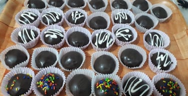 A tray of homemade chocolate truffles with white icing drizzle and colorful sprinkles in white paper liners.