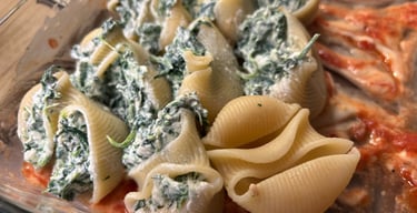 Stuffed pasta shells filled with spinach and ricotta cheese over marinara sauce in a glass baking dish.
