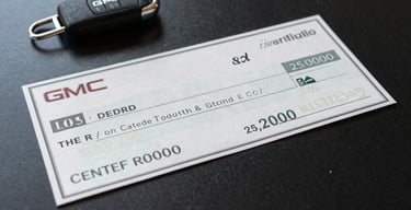 Close-up of a certified check for $25,000,000 resting on a polished matte black surface beside a GMC key fob, daylight from the left, crisp and tangible