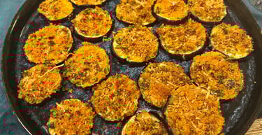 Crispy baked eggplant rounds topped with golden herb breadcrumbs on a black serving platter.