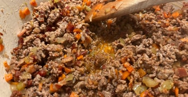 Browning ground beef with diced carrots and onions in a pot for a homemade bolognese sauce recipe.