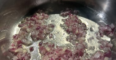 Finely diced red onions sautéing in oil inside a stainless steel pot.
