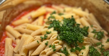 Penne pasta with tomato sauce and fresh parsley garnish in a stainless steel cooking pot.