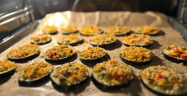 Baked eggplant rounds topped with breadcrumbs and herbs on a baking sheet inside a warm oven.