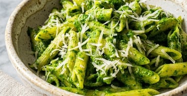 A bowl of penne pasta with vibrant green spinach pesto sauce and grated parmesan cheese.