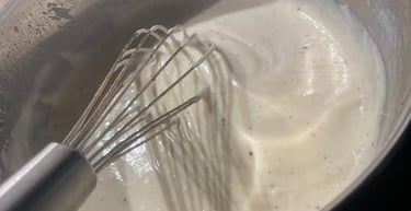 Pouring fresh milk into a pan with roux and a metal whisk to make homemade white sauce.
