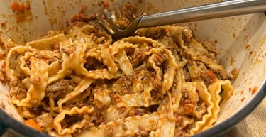 Homemade mafaldine pasta with hearty bolognese meat sauce in a white enameled dutch oven.