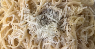 Freshly cooked cacio e pepe pasta topped with grated pecorino cheese and cracked black pepper.