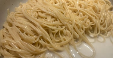 Freshly cooked linguine pasta tossed in a creamy white sauce with black pepper in a silver pan.