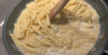 Cooking short pasta in a creamy sauce being stirred with a wooden spoon in a non-stick frying pan.
