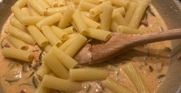 Cooked rigatoni pasta mixed into a creamy tomato zucchini sauce in a large skillet.