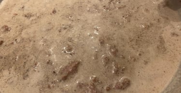 Homemade creamy sausage gravy simmering in a stainless steel skillet for a southern style breakfast.