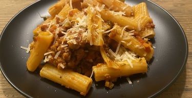 Rigatoni pasta with savory meat sauce and shredded parmesan cheese on a black plate.