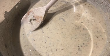 A wooden spoon stirring a creamy, savory peppercorn sauce or mushroom gravy in a stainless steel pot.