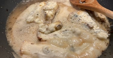 Gorgonzola cheese melting into a creamy white sauce in a skillet with a wooden spoon.