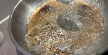 Deglazing a stainless steel pan with liquid to make a flavorful pan sauce.