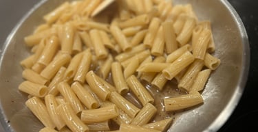 Rigatoni pasta cooking in a stainless steel skillet with butter sauce and pepper.