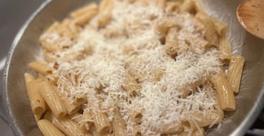 Rigatoni pasta with grated Pecorino cheese and black pepper in a stainless steel pan.