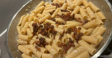 Rigatoni pasta alla Gricia with crispy guanciale and creamy egg sauce in a stainless steel pan.