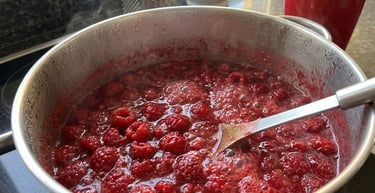 Fresh red raspberries simmering in a stainless steel pot while making homemade raspberry jam.
