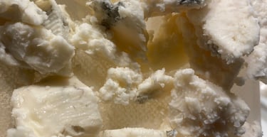 Crumbled pieces of gourmet blue cheese showing edible mold veins on a white cutting board.
