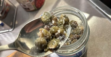 A metal spoon scooping salt-cured capers from a glass jar for Mediterranean cooking.
