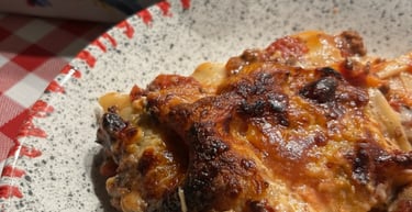 A portion of homemade beef lasagna with melted cheese on a plate over a red checkered tablecloth.