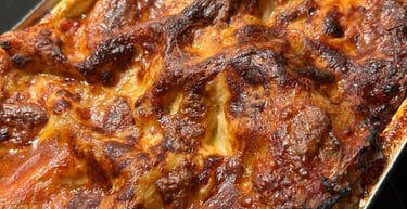 A close-up, top-down view of a freshly baked, bubbling, golden-brown lasagna with crispy cheese and rich tomato sauce