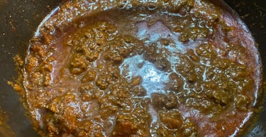Rich and chunky homemade bolognese sauce simmering in a black pot, featuring ground beef and tomato base.