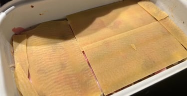 Uncooked lasagna layered with pasta sheets, ham, and sauce in a white baking dish, ready for baking.