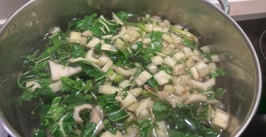 Fresh chopped bok choy simmering in a stainless steel pot of water for a healthy vegetable soup.