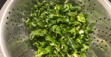 Freshly chopped green leafy vegetables being washed in a stainless steel kitchen colander.