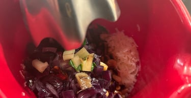 Mixing chopped red onions and pine nuts in a red bowl with an immersion blender to make pesto.