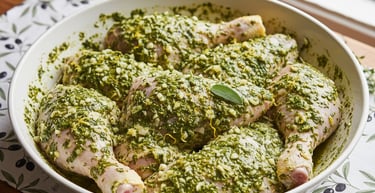Raw chicken drumsticks coated in a green herb and garlic marinade in a white bowl.