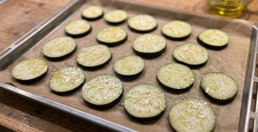 Sliced eggplant rounds brushed with olive oil on a baking sheet with parchment paper for roasting.