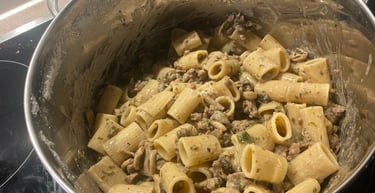 A stainless steel pot filled with cooked rigatoni pasta, ground meat, and mushrooms in a creamy sauce.