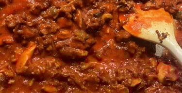 Homemade chunky pasta meat sauce with ground beef and tomatoes simmering in a large pot with a wooden spoon.