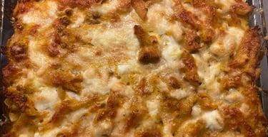 Golden brown baked penne pasta casserole topped with melted mozzarella cheese in a glass baking dish.