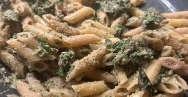 Healthy whole grain penne pasta tossed with fresh green spinach pesto sauce in a skillet.