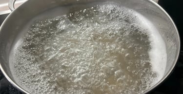 A large stainless steel pot filled with rapidly boiling water on a kitchen stove.