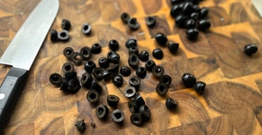Sliced black olives on a rustic wooden cutting board with a chef's knife for food preparation.