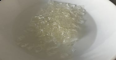 Clear gelatin sheets blooming in a white bowl of water for a dessert recipe.