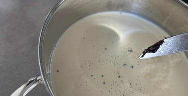 Fresh vanilla bean seeds scraped into a stainless steel pot of heavy cream for cooking.