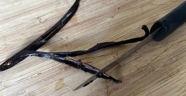 A pairing knife slicing open fresh gourmet vanilla beans on a wooden cutting board.