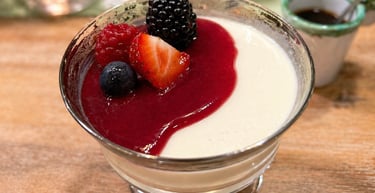 Creamy Italian panna cotta dessert topped with red berry coulis and fresh mixed berries in a glass bowl.